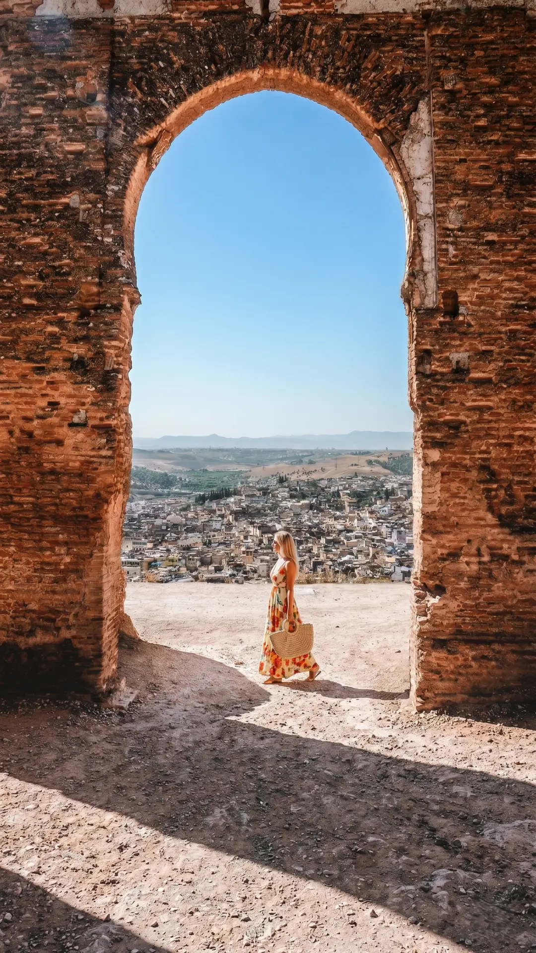 Woman in floral dress at ancient brick arch overlooking the sprawling Fez Medina and hills in Morocco