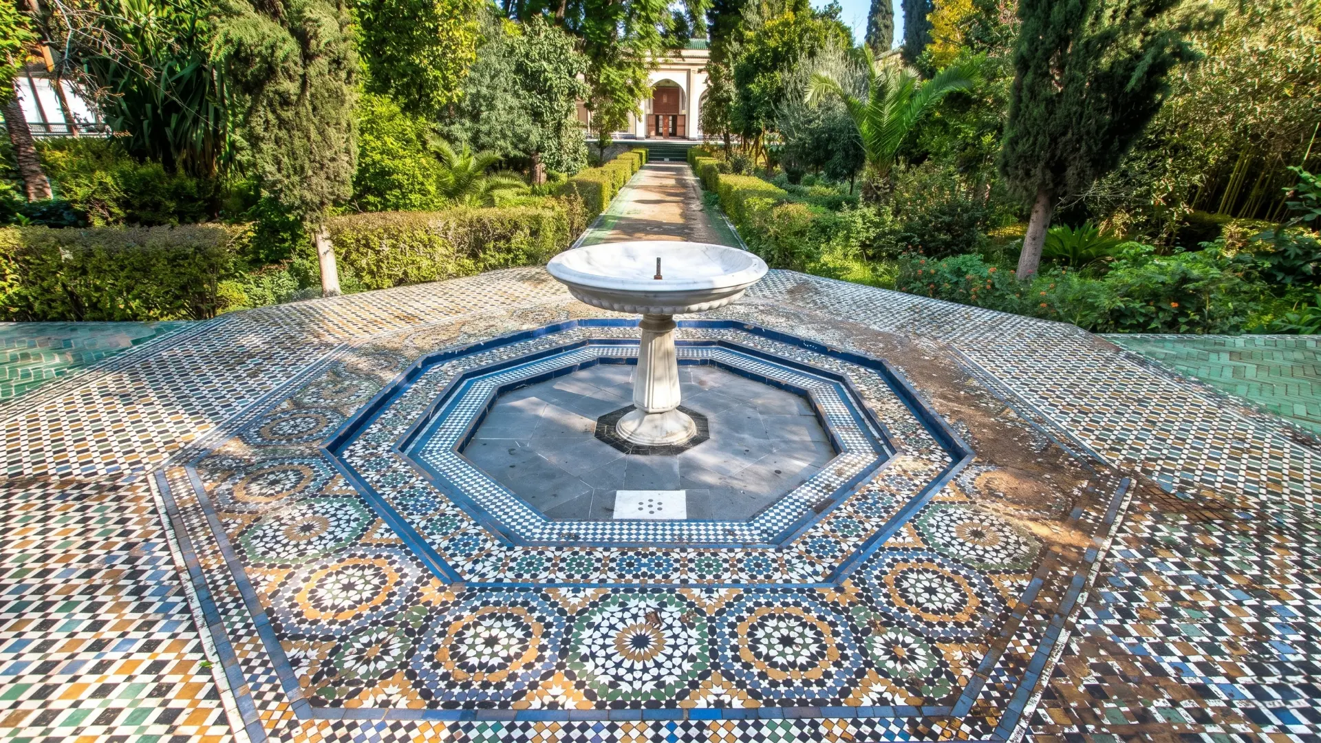 Colorful geometric zellige mosaic fountain with intricate star patterns and ornate arch in the gardens of Dar Batha Museum, Fez Morocco